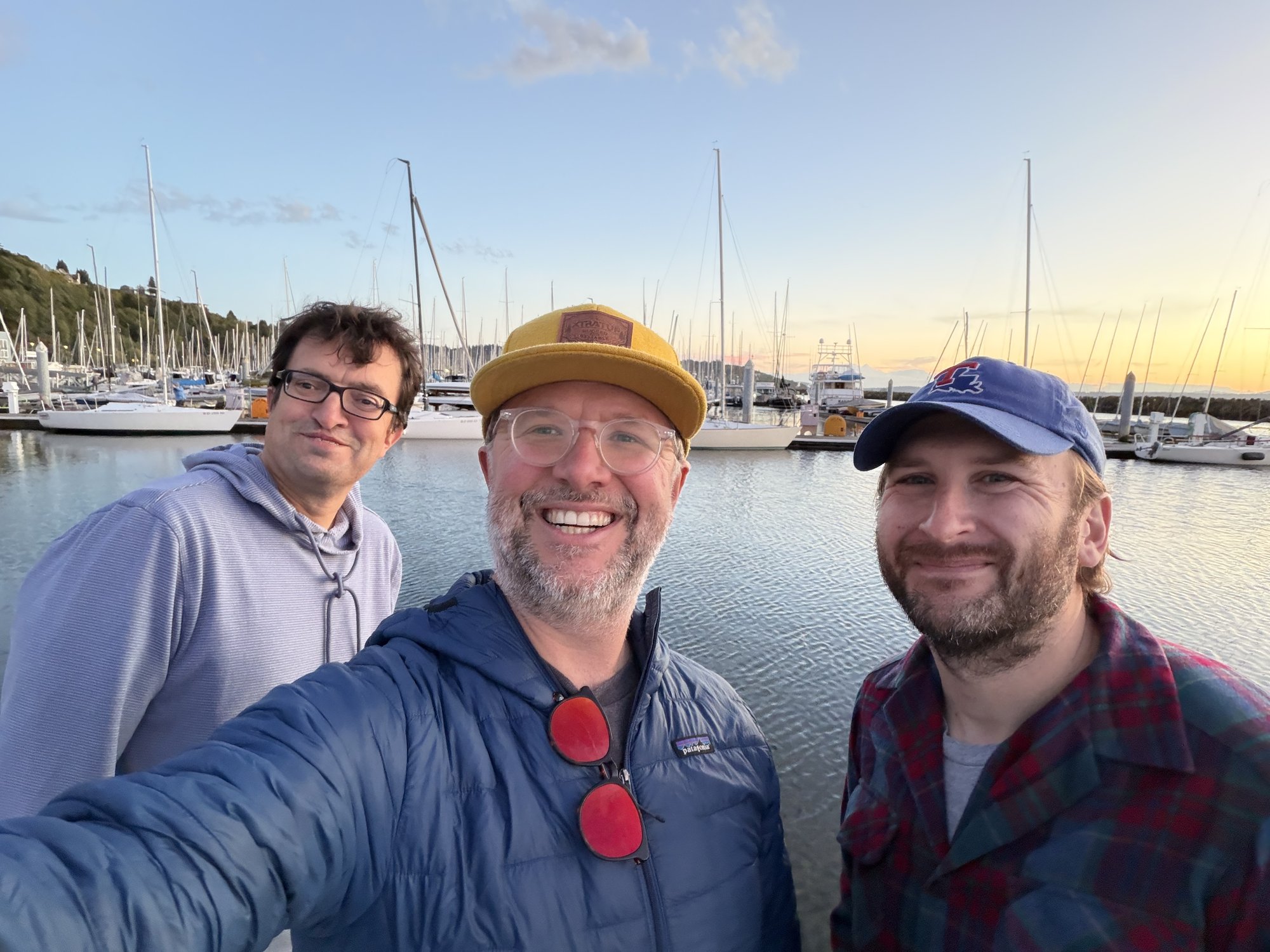 Three sailors smiling for a selfie on the docks at Shilshole Bay Marina at sunset