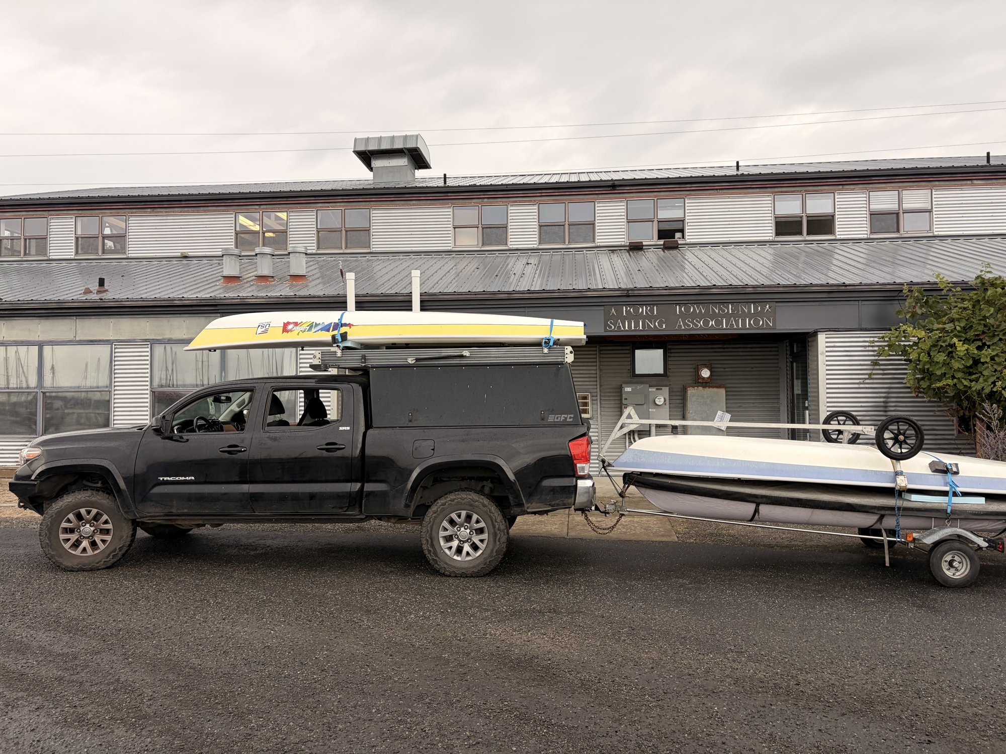A pickup truck with a Laser on the roof rack towing a trailer stacked with two more Lasers, parked outside PTSA